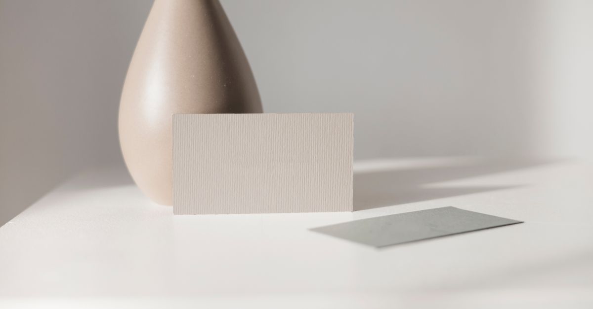 Elegant minimalist mockup featuring a blank card and ceramic vase on a white table. Perfect for branding or design.